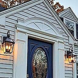 Elegant pediment accentuating a classic entryway, framed by stylish wall sconces, showcasing architectural beauty and inviting ambiance against a serene backdrop.