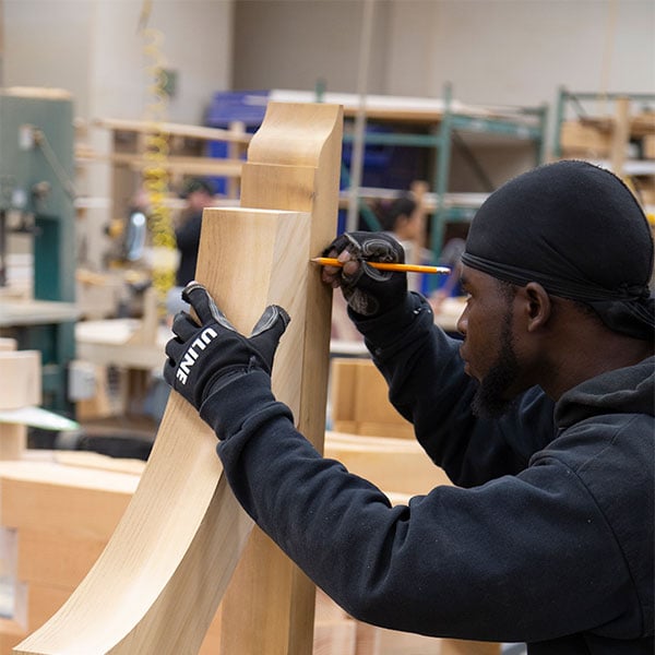 Craftsman focuses intently on shaping custom woodwork, showcasing expert craftsmanship in a workshop filled with tools and materials, embodying the artistry of bespoke furniture creation.