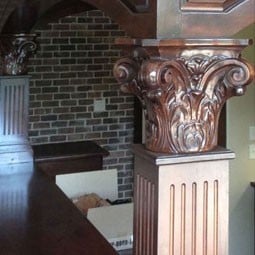 Intricately carved wooden capital showcasing classic architectural design, complementing a rustic brick backdrop. Perfect blend of elegance and craftsmanship in interior spaces.