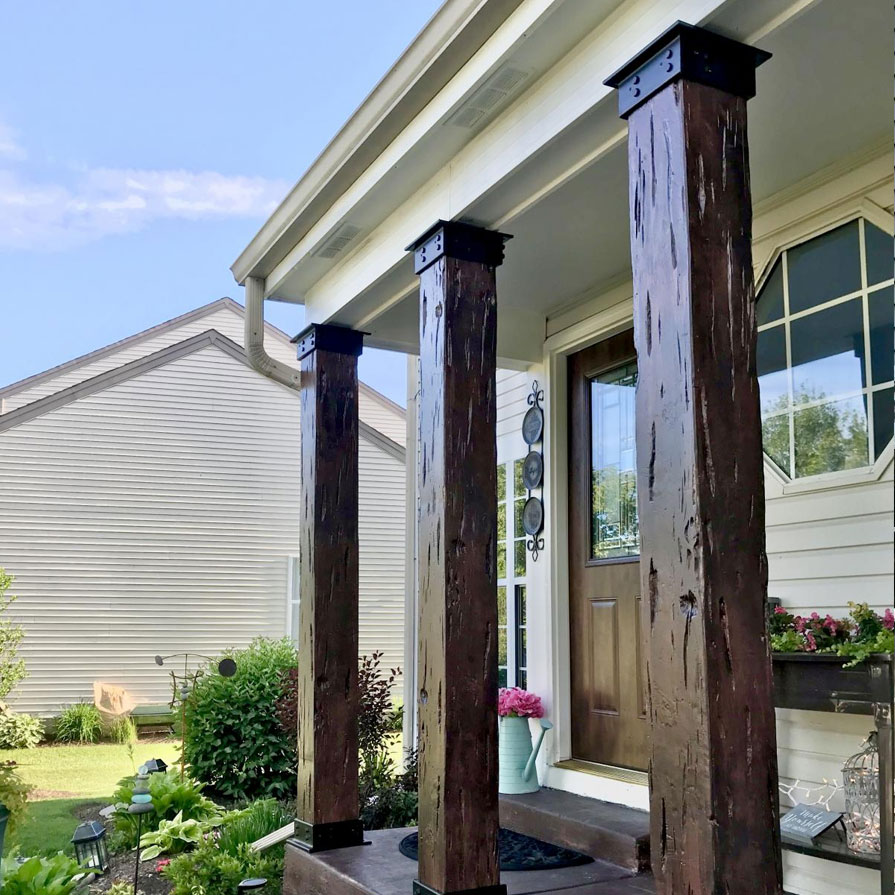 Rustic wooden columns support a charming porch entrance, framed by lush greenery and inviting floral arrangements, adding character and style to the home's facade.