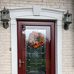 Elegant entryway featuring a decorative crosshead with keystone above a red door, framed by vintage lanterns and adorned with a seasonal wreath, enhancing curb appeal.
