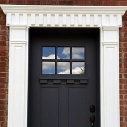 Architectural detail of a stylish black door framed by an elegant white crosshead trim against a brick wall, enhancing curb appeal and providing a welcoming entrance.