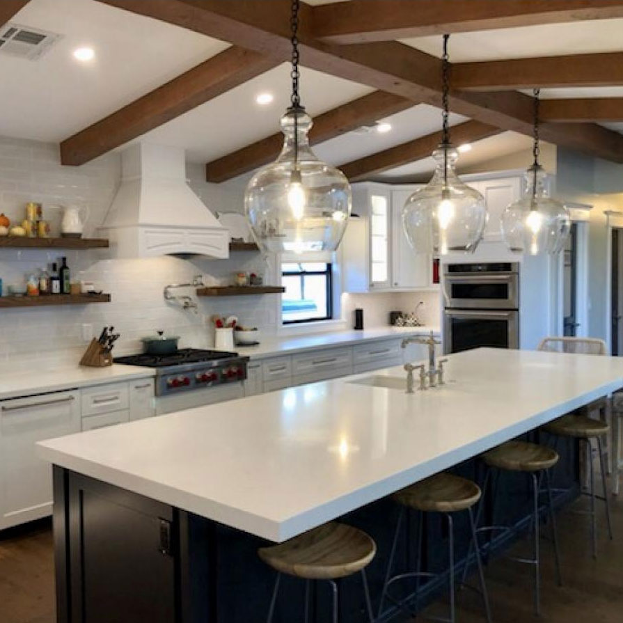 Bright and inviting kitchen featuring decorative millwork, exposed beams, and modern pendant lights, highlighting a stylish blend of rustic and contemporary design elements.