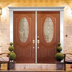 Elegant double doors with decorative oval glass panels, framed by stylish trims, enhance a welcoming entrance against a warm brick facade and complementary landscaping.