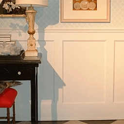 Elegant room featuring wainscot paneling and a contrasting dark furniture piece. Soft blue walls and decorative lamp add a cozy, sophisticated ambiance. Perfect for interior design inspiration.